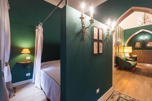 Ein Schlafzimmer mit einem Bett, einem Nachttisch, einer Lampe, einem grünen Sessel und einer Kronleuchter.