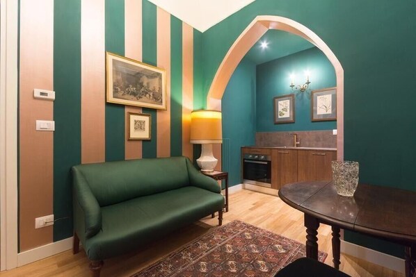 A living room with a green sofa, a small table, and a kitchen area visible through an archway. - Porta Palace Apartments (Turin)