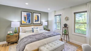 A bedroom with a large bed, two bedside tables, a window with a view, and abstract art on the wall.