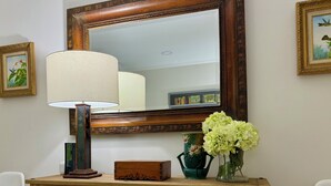A wooden dresser with a mirror above it, a lamp, a vase with flowers, and framed pictures on the wall.