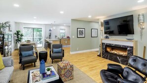 A spacious living room with a fireplace, a large TV, and a dining area with a view to the outside.