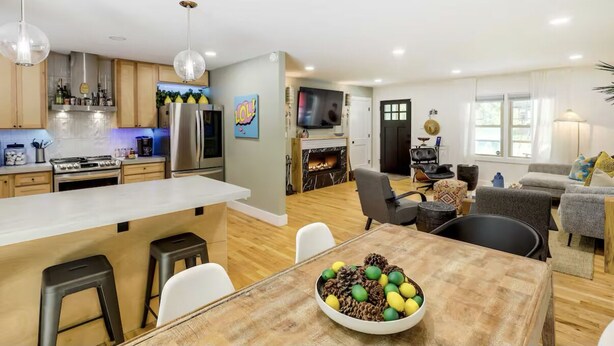 A modern kitchen with a large island, a dining area with a wooden table, and a living room with a fireplace.