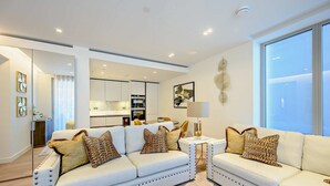 A modern living room with a white sofa set, a small side table, and a large window providing natural light. - Contemporary Marylebone with Pool and Gym AC (Greater London)