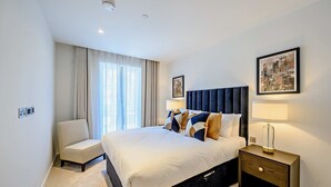 Una habitación de hotel con una cama grande, una mesita de noche con lámpara, una silla y una ventana con cortinas.