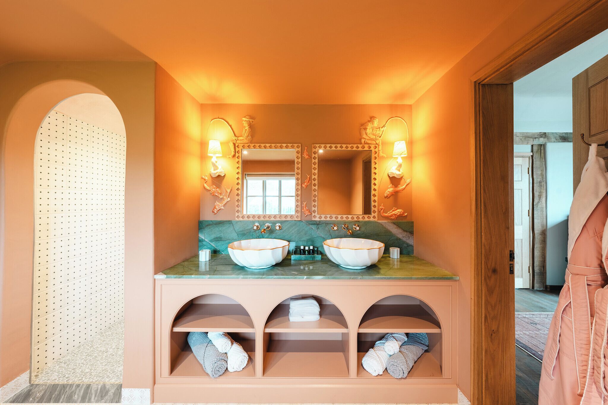 A bathroom with two large, oval-shaped sinks, a mirror with wall sconces, and a towel rack.