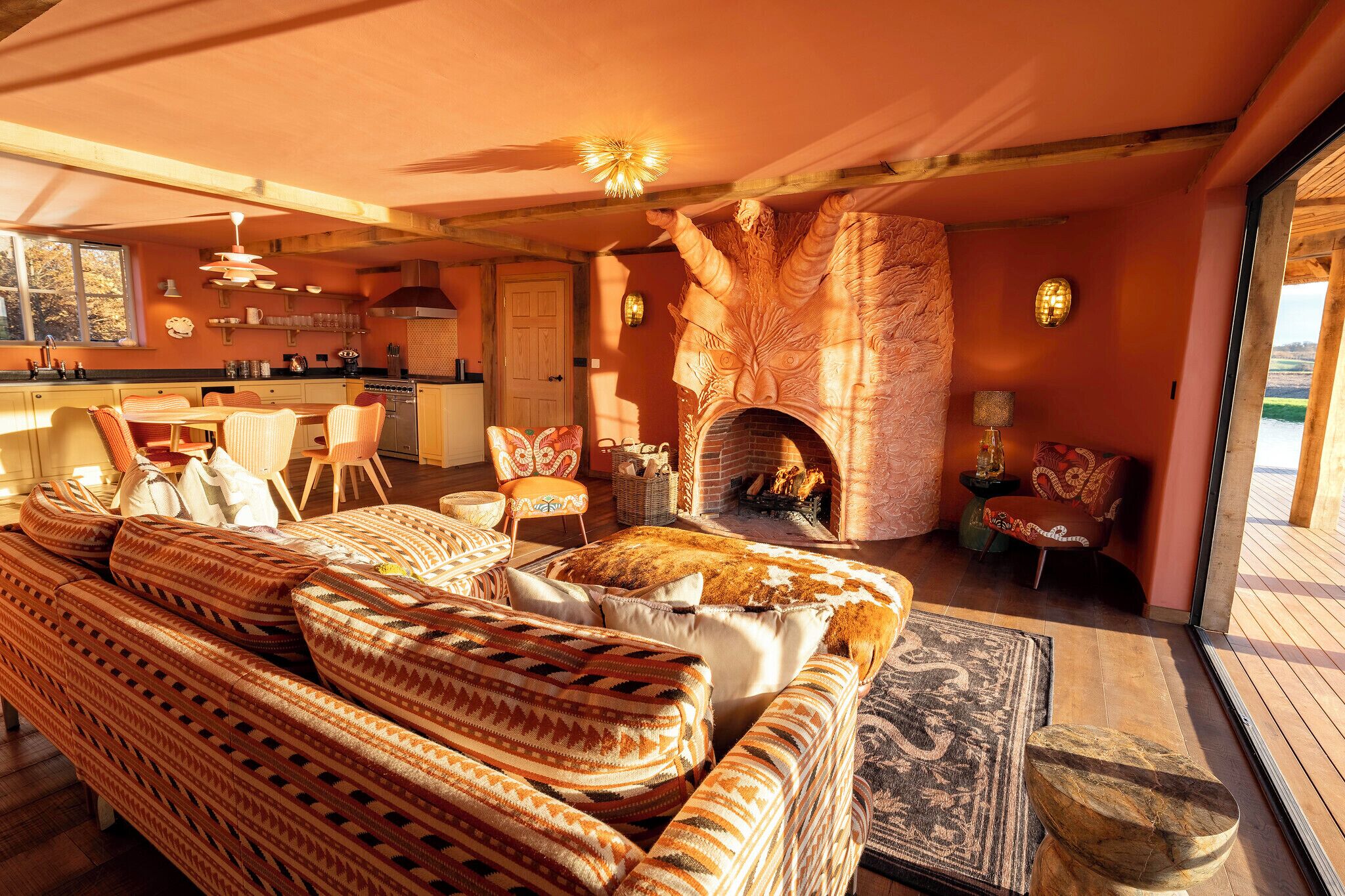 A cozy living area with a fireplace, comfortable seating, and a kitchen in the background.