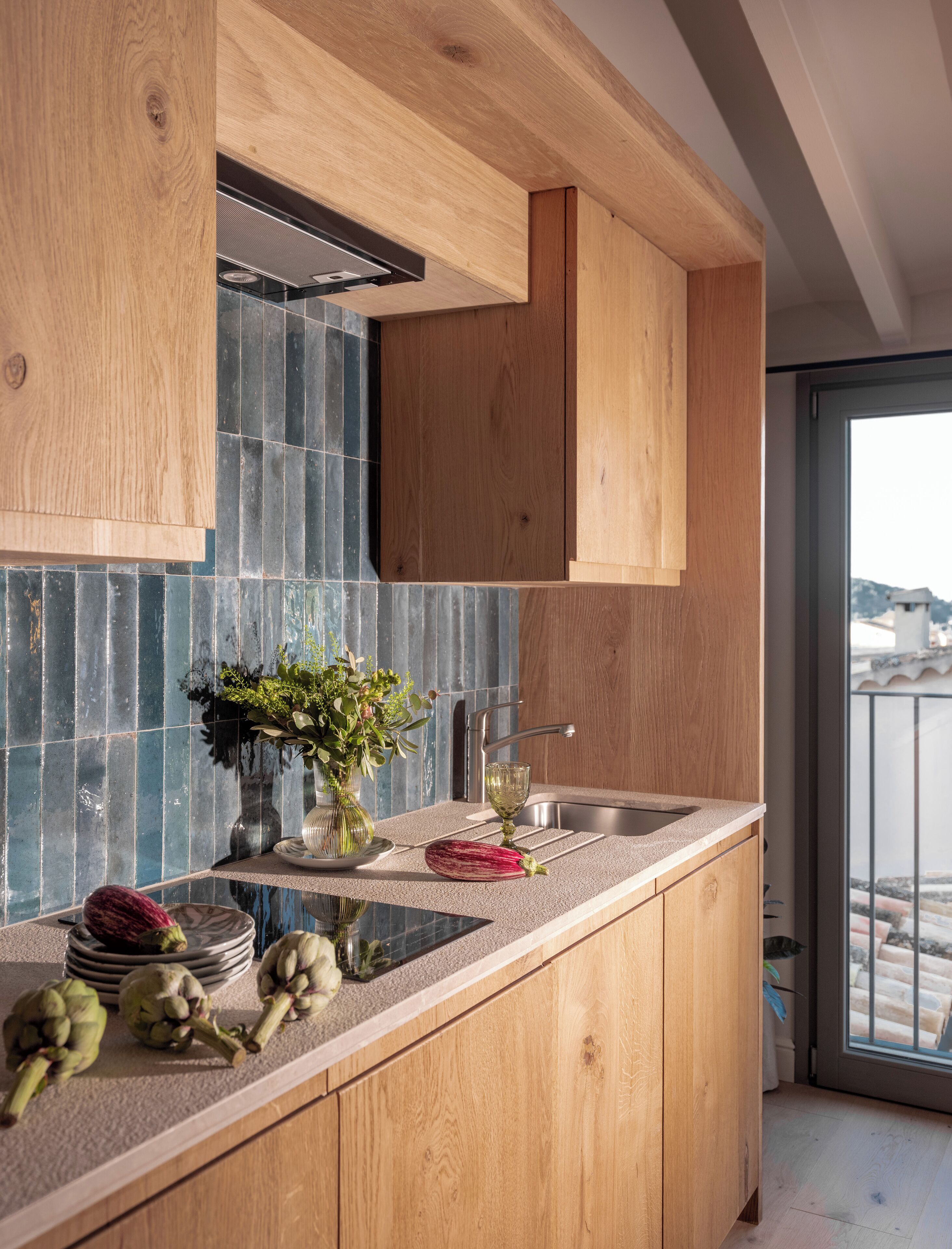 Una cocina moderna con armarios de madera, salpicadero de azulejos y vistas a la ciudad a través de un ventanal amplio.