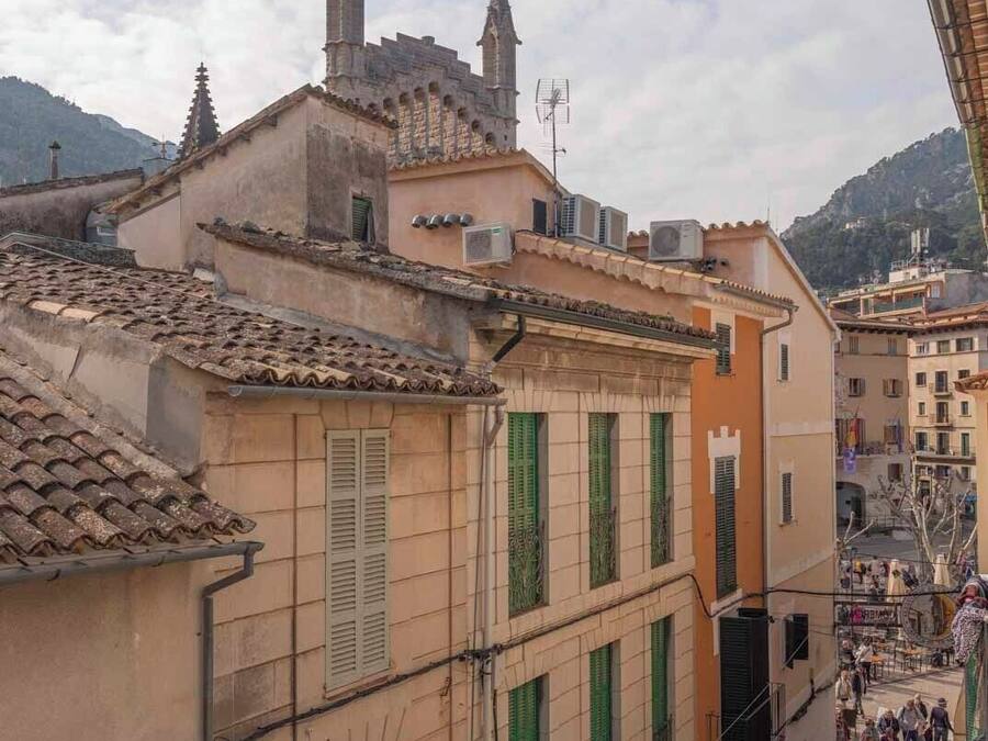 A street view with buildings featuring traditional architecture, including terracotta roofs and green shutters.