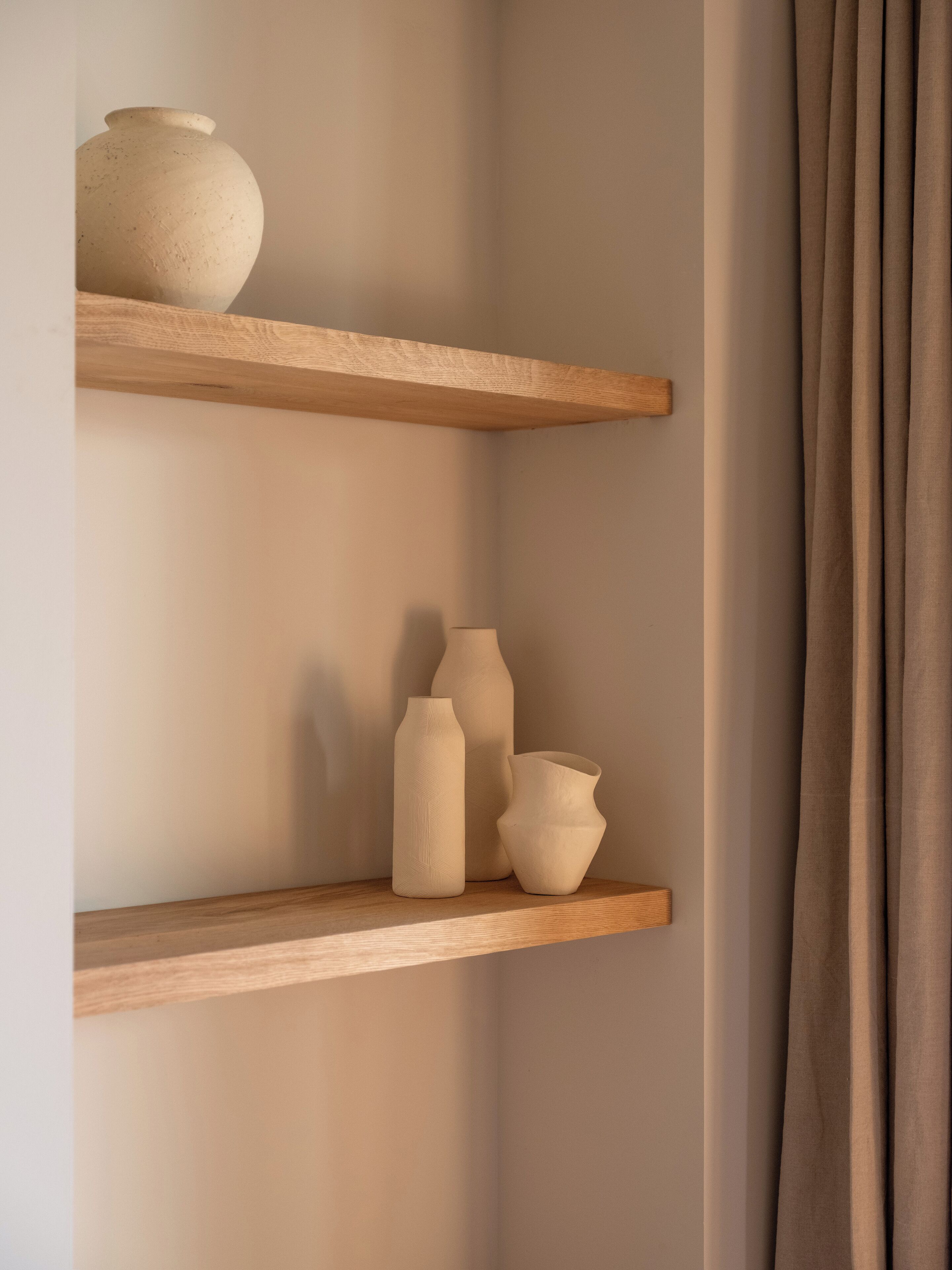 Two wooden shelves with ceramic vases against a plain wall.