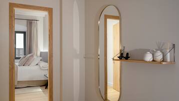 A modern bedroom with a wooden door leading to a balcony, a round mirror on the wall, and a shelf with decorative items.