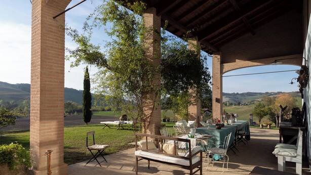 An outdoor patio with a brick column, a wooden bench, and a table set for dining. - CASA DELLE VIOLE (Fornovo di Taro)