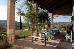 An outdoor patio with a brick column, a wooden bench, and a table set for dining. - CASA DELLE VIOLE (Fornovo di Taro)