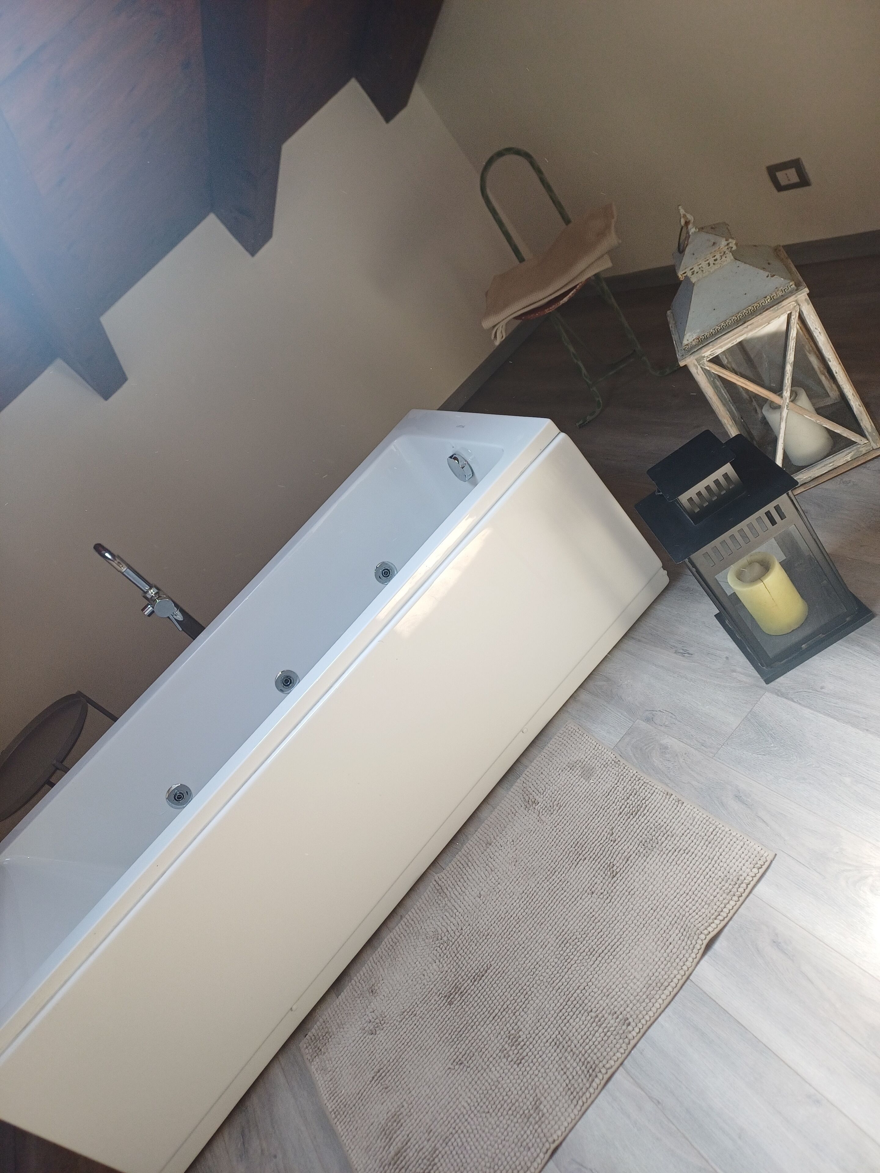 A bathroom with a white bathtub, a wooden floor, a beige rug, a lantern, and a towel rack.