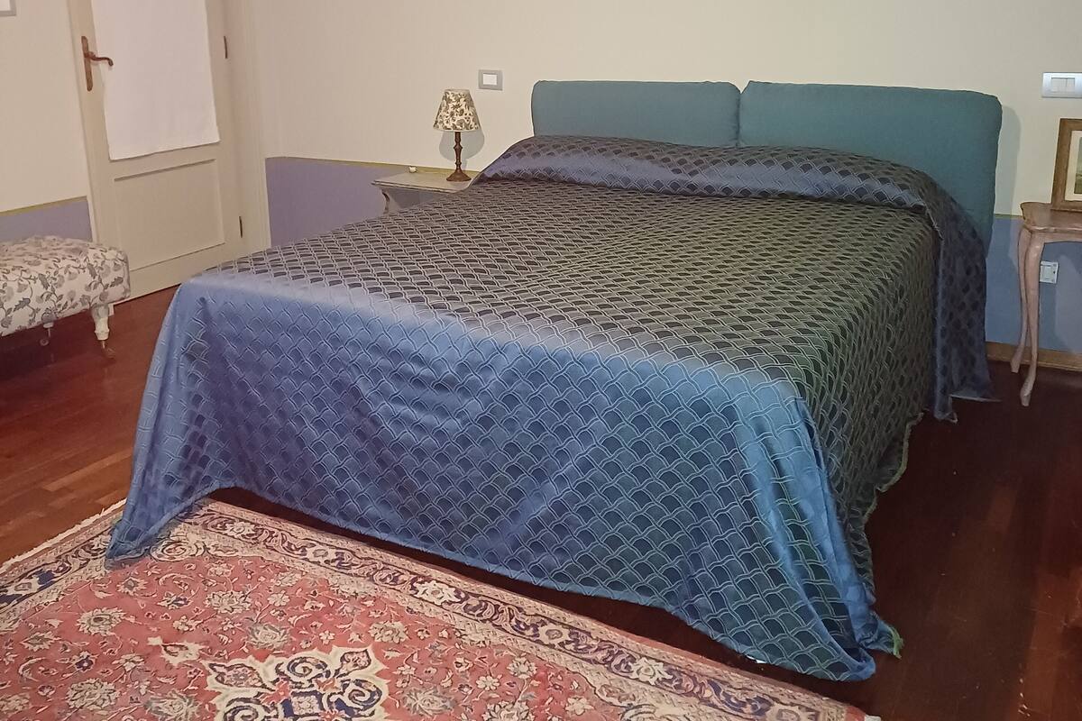 Makuuhuone, jossa on sänky, yöpöytä, lamppu, seinällä oleva kehystetty kuva ja ovi.