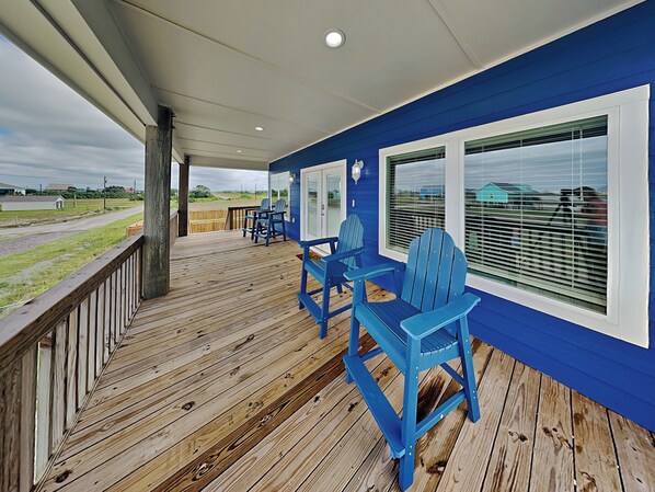 A covered porch with blue Adirondack chairs, a wooden deck, and a view of the surrounding landscape.