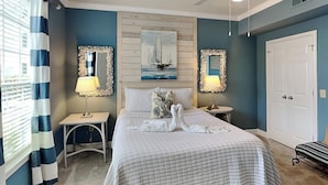 A neatly arranged bedroom with a large bed, two bedside tables with lamps, a headboard with a painting, and a door. - Coastal Cabana | Beautiful Views + 2 Pools (Galveston)