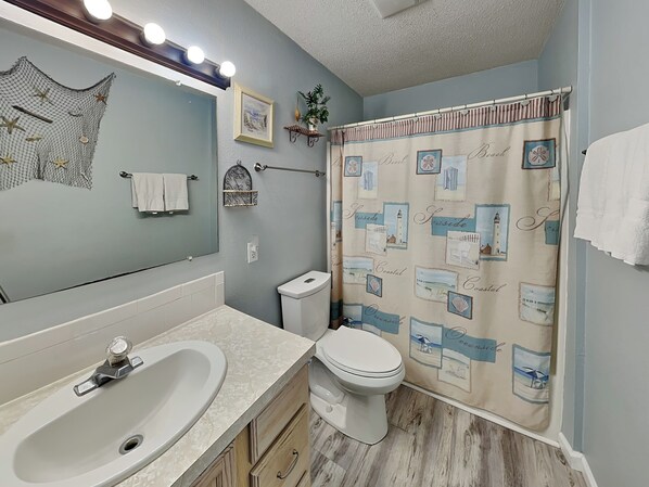 A bathroom with a sink, toilet, and shower curtain with coastal designs.