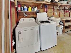 A laundry area with two stacked washers and dryers, a shelf with cleaning supplies, and an American flag.
