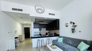 Une cuisine moderne avec des meubles de couleur sombre, un îlot central blanc et un canapé gris dans l’espace salon.