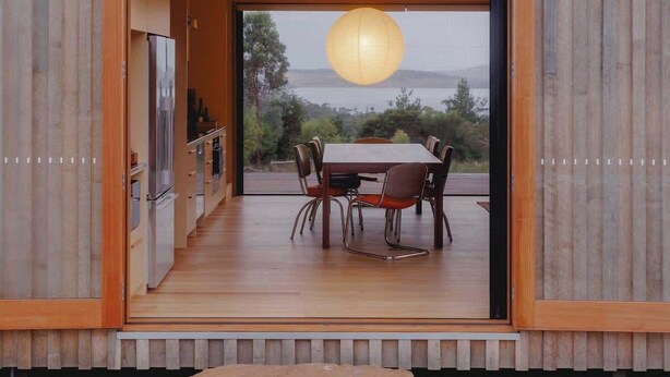 A modern house with a wooden exterior, a dining area with a table and chairs, and a view of the outdoors. - Hidden Spring Beach S (Spring Beach)