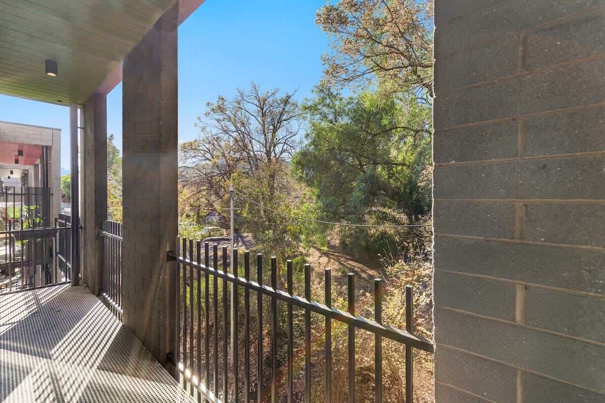 A balcony with a metal railing overlooking a landscaped area with trees and a brick wall.