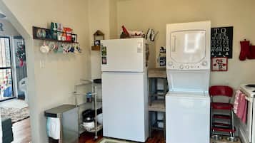 Eine kompakte Küche mit Kühlschrank, Waschmaschine und kleinem Mülleimer.