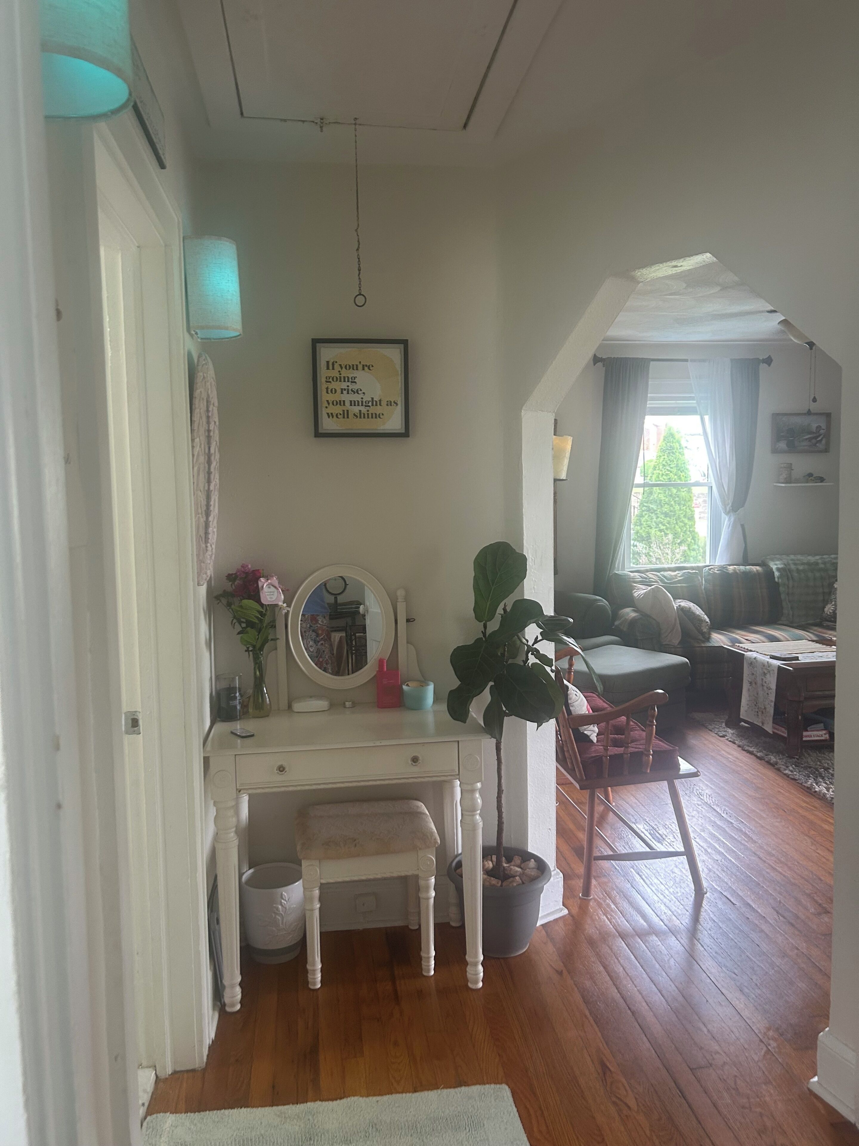 Une pièce avec un bureau blanc, un miroir, une plante en pot et une vue sur l’extérieur par une fenêtre.