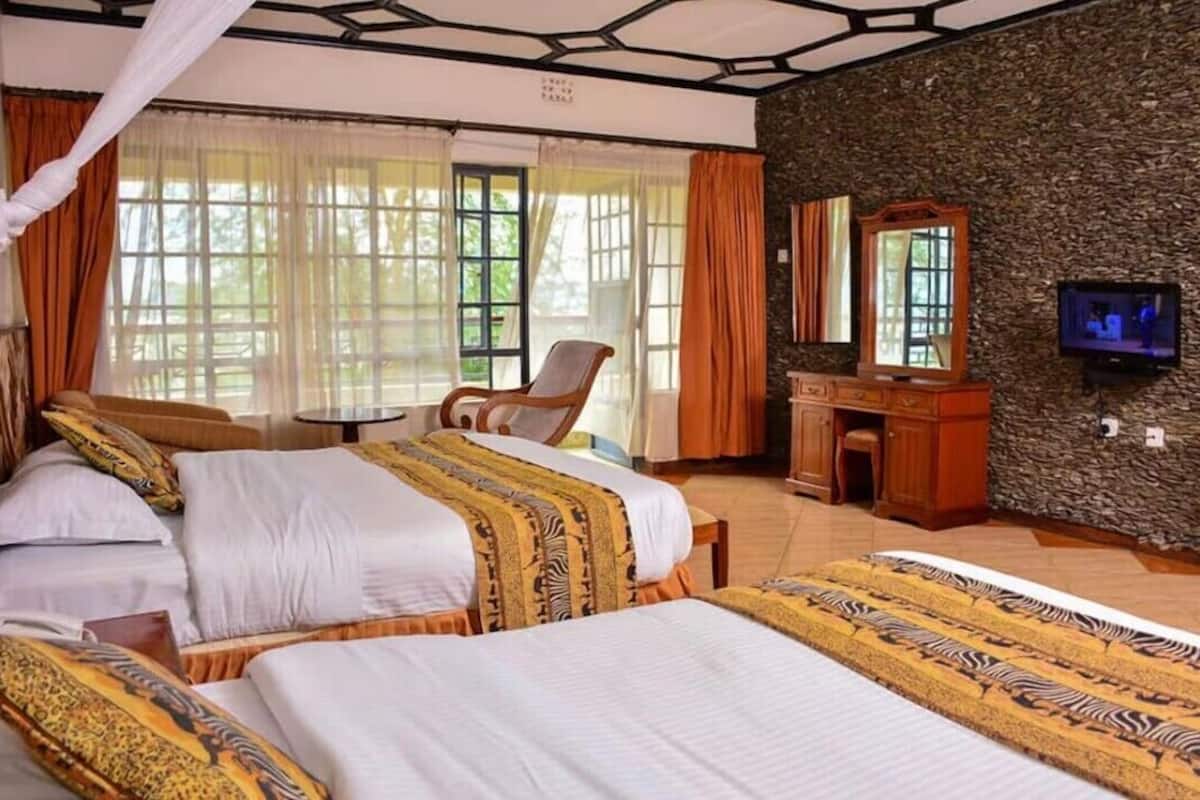 A hotel room with two beds, a sitting area, a television, and a stone wall.