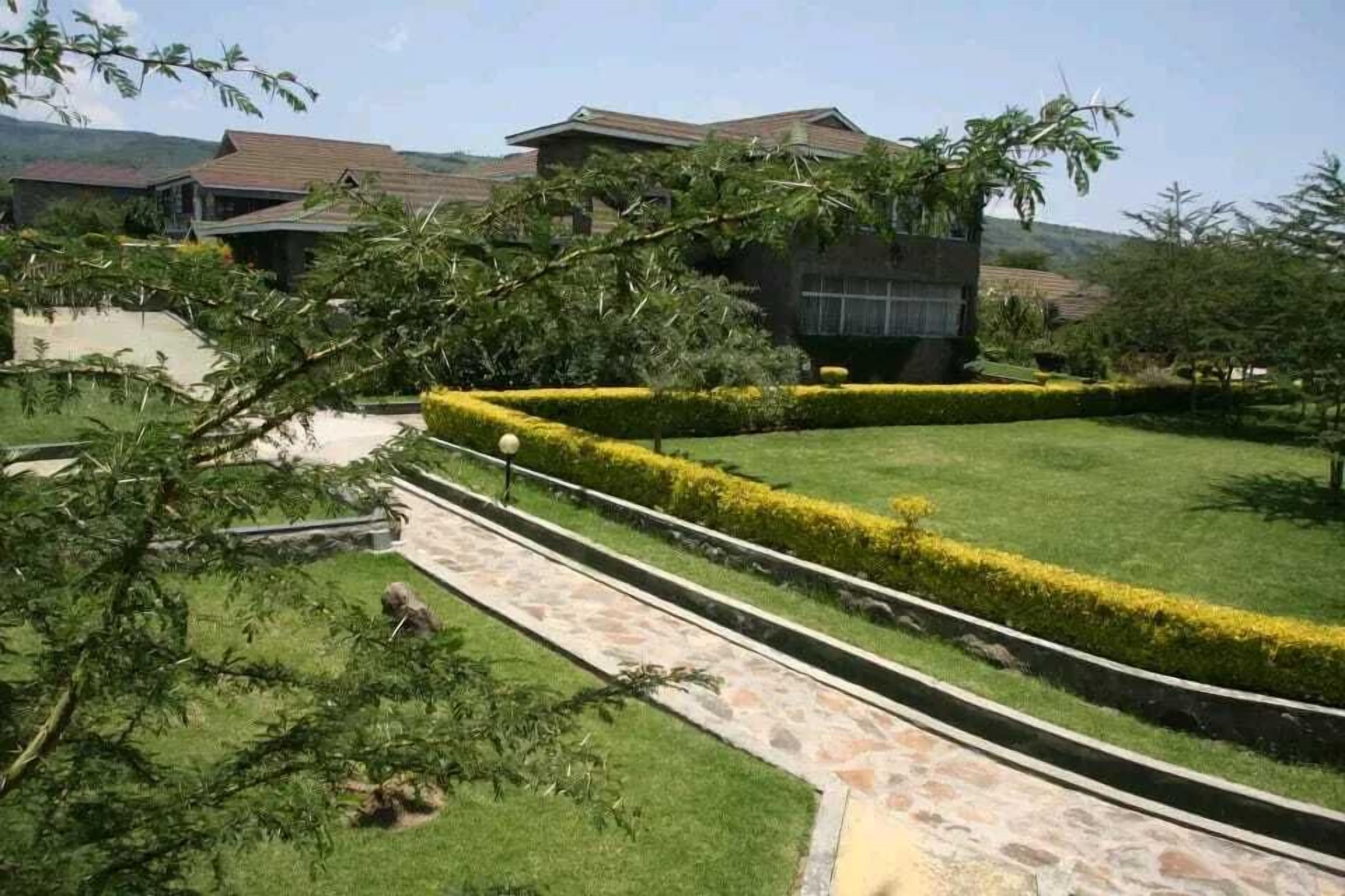 A well-maintained garden with a stone pathway, neatly trimmed hedges, and a building with a tiled roof in the background.