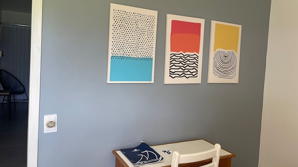 A room with a grey wall, a wooden table with a chair, and three artworks. - Grande Lago Hotel Gastronomia Bar (Três Marias)