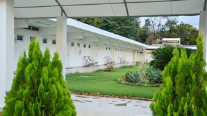 A covered outdoor area with a white building, green lawn, and potted plants. - Grande Lago Hotel Gastronomia Bar (Três Marias)