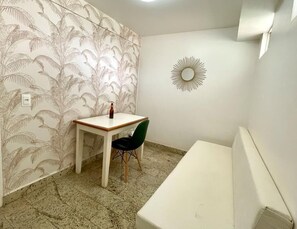 Una habitación pequeña con papel tapiz estampado, un espejo redondo, una mesa con una botella y una silla.