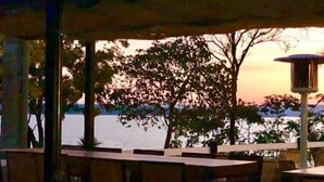 An outdoor seating area with tables and chairs, overlooking a body of water and trees. - Grande Lago Hotel Gastronomia Bar (Três Marias)