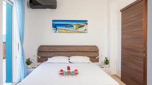 A bedroom with a wooden headboard, a bed with white bedding, a painting of a coastal scene, and a tray of flowers on the bed. - Laftira's Sea View Home (Stegna)