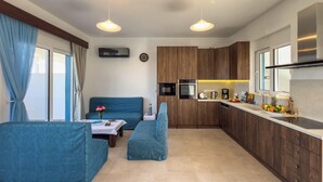 A modern kitchen with wooden cabinets, a built-in oven, and a coffee maker. There is a dining area with blue upholstered furniture and a small table with a vase of flowers. - Laftira's Sea View Home (Stegna)