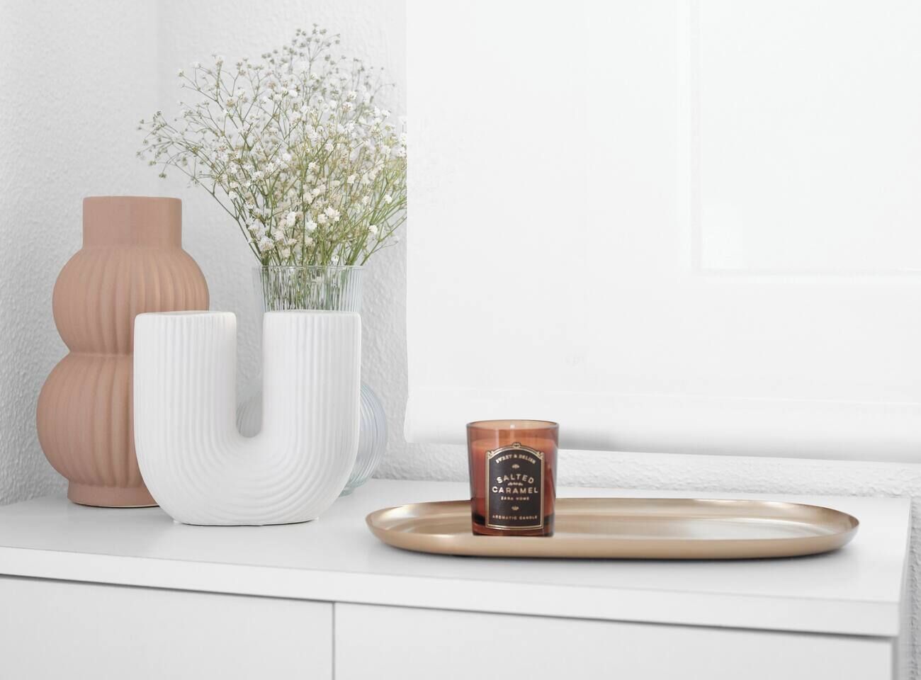 A white vase with flowers, a candle, and a tray on a white surface.