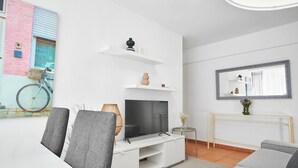 Un salon moderne doté d’un téléviseur à écran plat, d’un meuble de rangement blanc, d’un canapé gris et d’une petite table d’appoint sur laquelle est posé un vase.