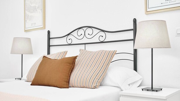 Un lit bien fait, agrémenté d’un ensemble d’oreillers blancs et rayés, d’un coussin décoratif marron et d’un oreiller blanc. Deux tables de chevet avec des lampes sont placées de chaque côté du lit.