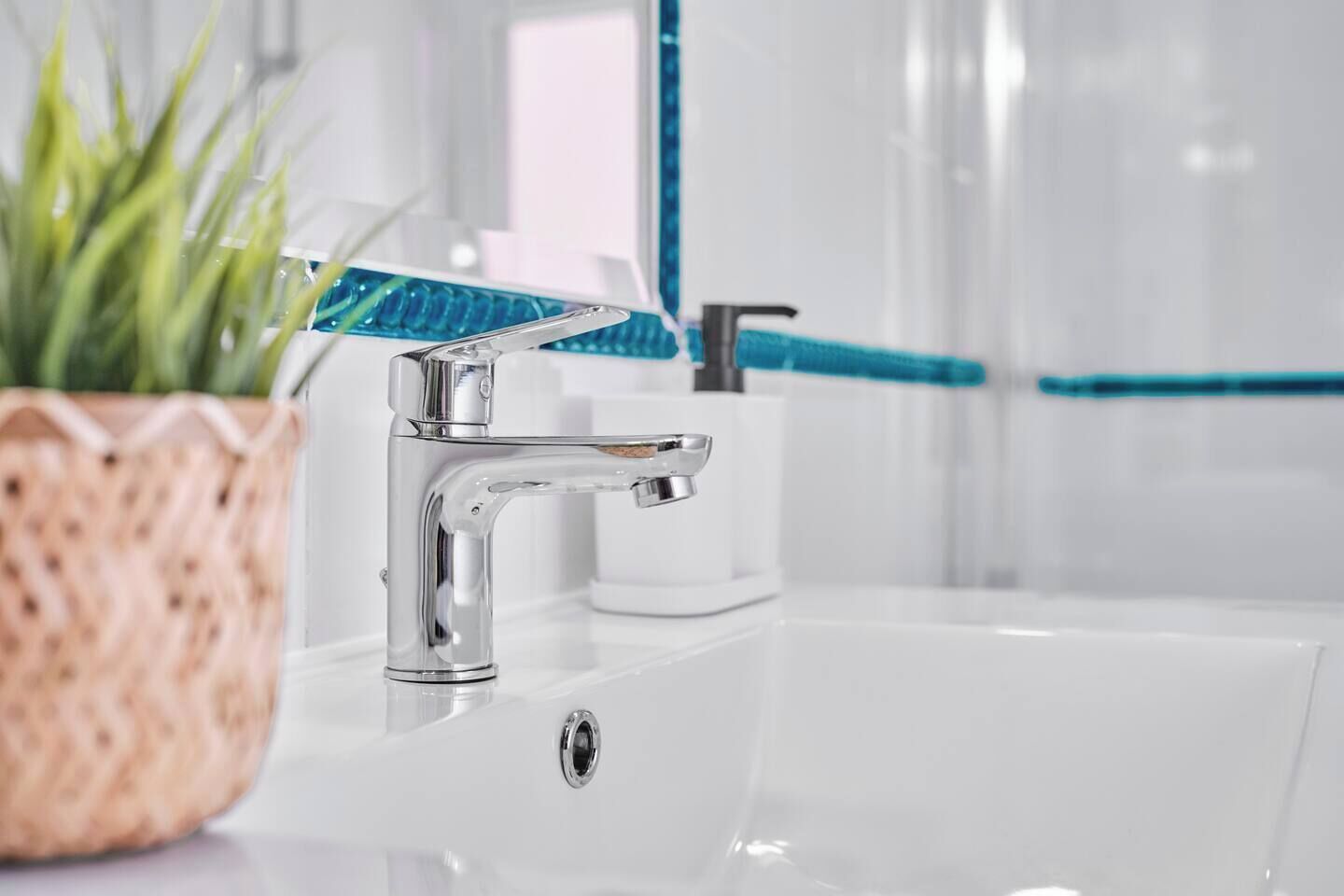 Un bany modern amb un aixeta cromada, un envàs de vidre blanc i un suport blau per al raspall de dents.