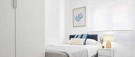 A bedroom with a bed, bedside table, lamp, and a framed picture on the wall.