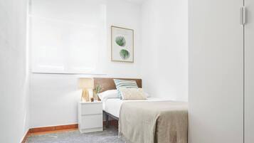 Un dormitorio con una cama, una mesita de noche, una lámpara, un cuadro enmarcado y una ventana.