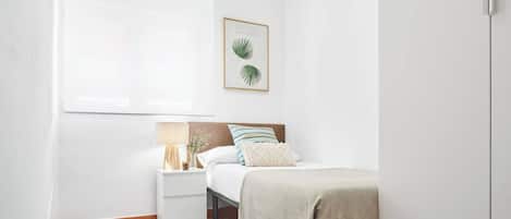 Een slaapkamer met een bed, een nachtkastje, een lamp, een ingelijste foto en een raam.