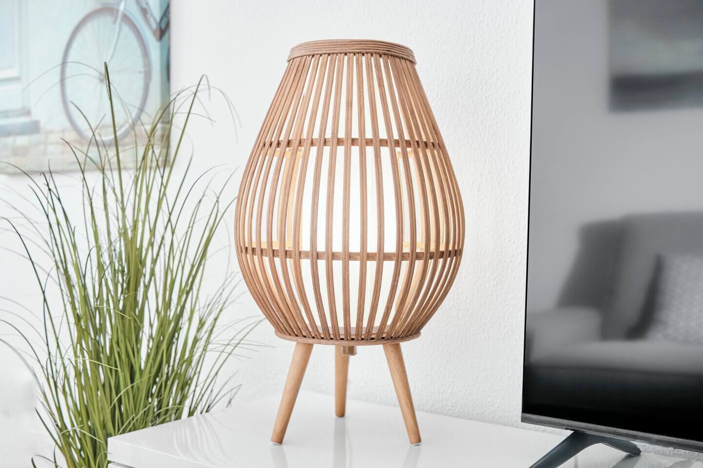 A wicker lamp with a cylindrical shape and a wooden base on a white surface.