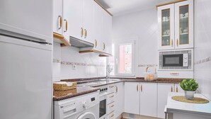 Une cuisine moderne avec des meubles blancs, un lave-linge encastré, un four à micro-ondes et une fenêtre laissant entrer la lumière naturelle.