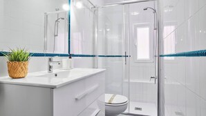 Une salle de bain moderne avec une douche à parois de verre, des accessoires blancs et une bordure de carreaux à rayures bleues.