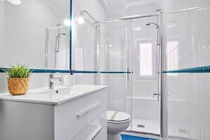 A modern bathroom with a glass-enclosed shower, white fixtures, and a blue-striped tile border. - Pinares by Wehomes Pinares Sardinero (Santander)