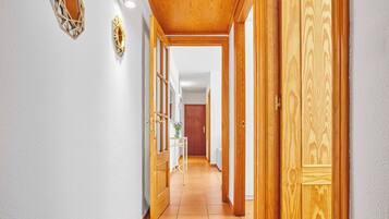 Un pasillo con puertas de madera y suelo de baldosas, que conduce a una habitación con una cama y una mesita de noche.