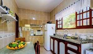 Una cocina con una mesa de comedor, refrigerador, microondas y una ventana con cortinas.