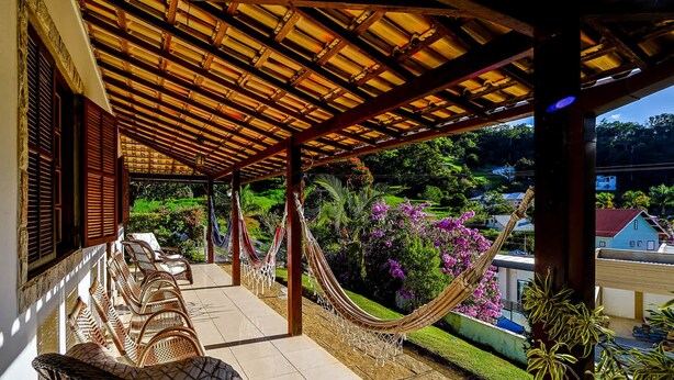 Un espace extérieur aménagé, abrité et doté d’un hamac, de meubles en osier, et offrant une vue sur un jardin luxuriant et des bâtiments situés au loin.