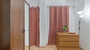 Ein Schlafzimmer mit einem Holzschrank, einem Nachttisch mit Lampe und zwei rosafarbenen Vorhängen.